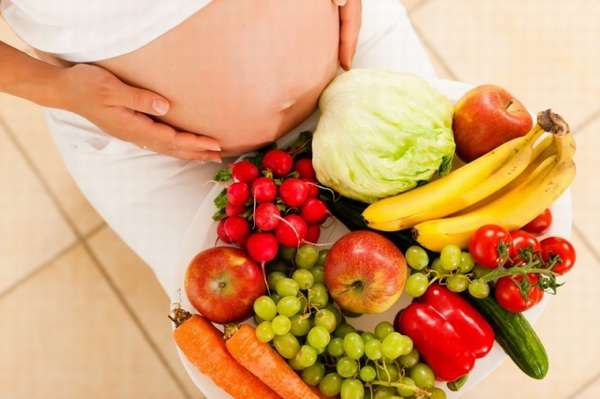 живот беременной и фрукты с овощами